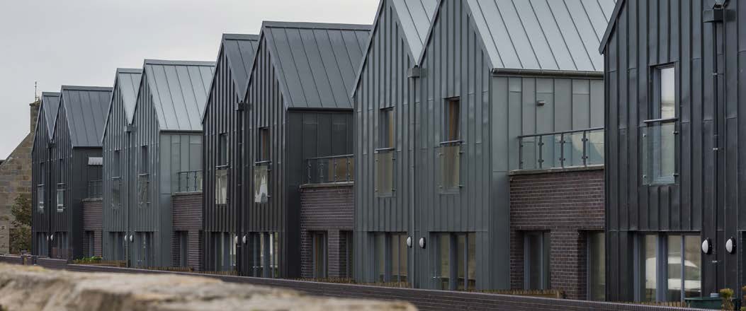 A row of interlocking houses in Fraserburgh with dark and light grey metal cladding and dark brick exterior walls beside each unit. 