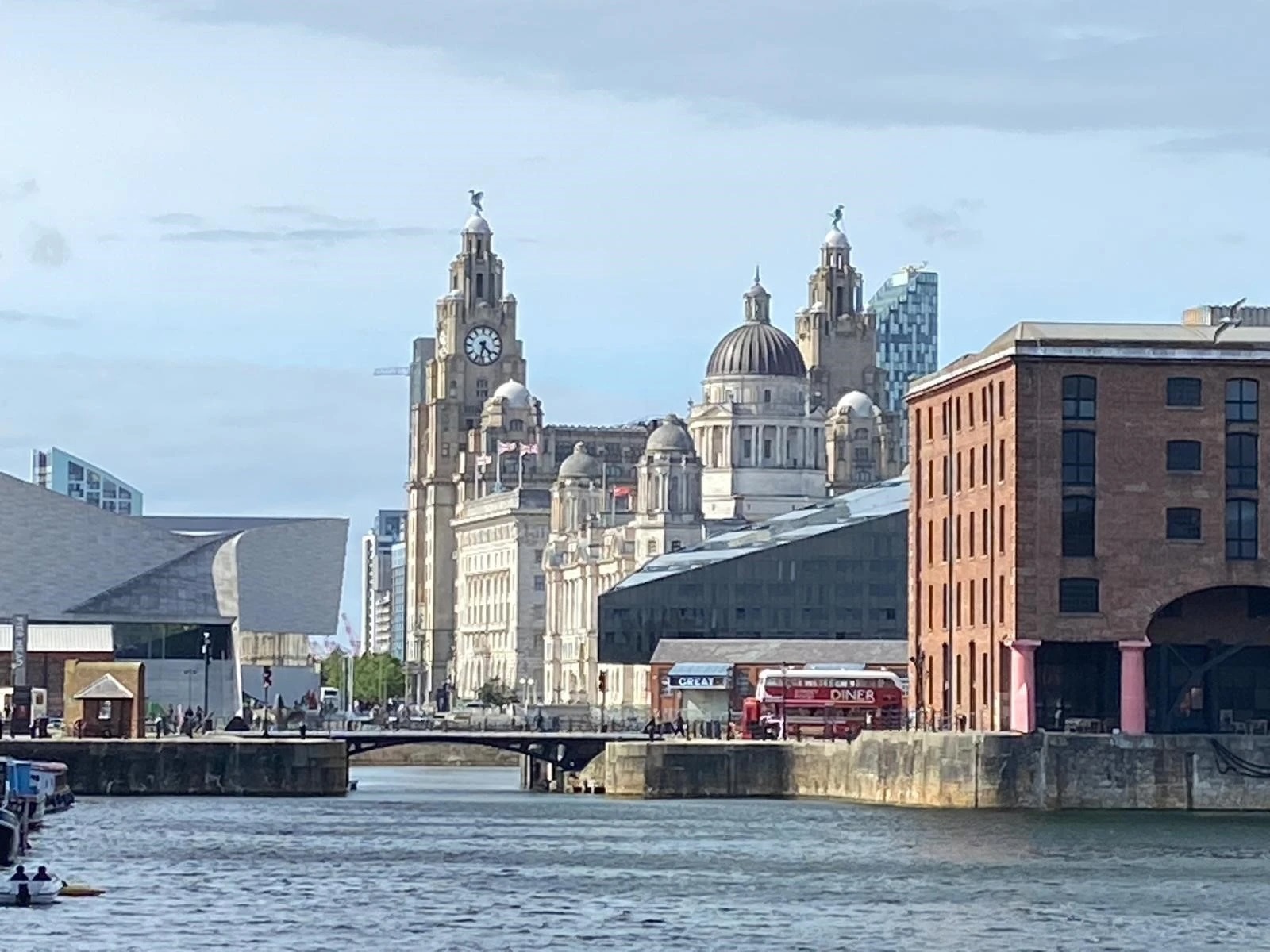 A photograph fo the river Mersey in Liverpool with buildings on both sides of the image and a brick buildingin in the foreground